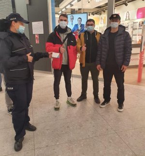 Policjantka trzyma w ręce maseczki obok niej stoi trzech mężczyzn z maskami zasłaniającymi usta i nos