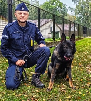 Zdjęcie przedstawia psa służbowego, obok stoi policjant.