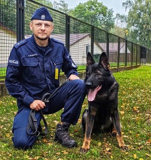 Zdjęcie przedstawia psa służbowego, obok stoi policjant.