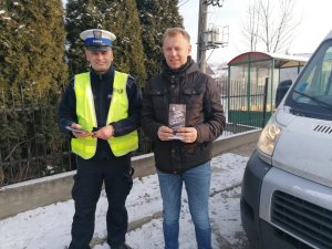 Policjant stoi z mężczyzna na przestanku autobusowym , w ręku trzymają ulotki