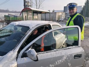 Policjant stoi przy pojedzie zatrzymanym do kontroli drogowej i rozmawia z kierującym o nowych przepisach