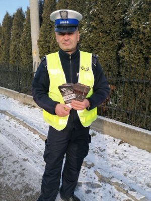 Policjant stoi na poboczu i trzyma w reku ulotki do rozdania