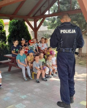 policjant stoi  tyłem, przed policjantem  siedzi  grupa dzieci