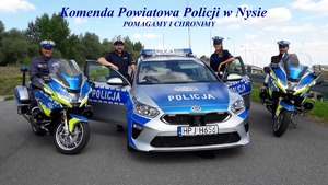 Na zdjęciu znajdują się policjanci Wydziału Ruchy Drogowego KPP w Nysie. Policjant i policjantka stoją przy radiowozie a dwóch policjantów siedzi na policyjnych motocyklach.