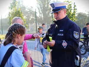 zdjęcie kolorowe: policjanci rozdają dzieciom kaski i elementy odblaskowe